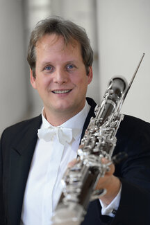 Henrik Rabien in Konzertkleidung mit einem Fagott in der Hand