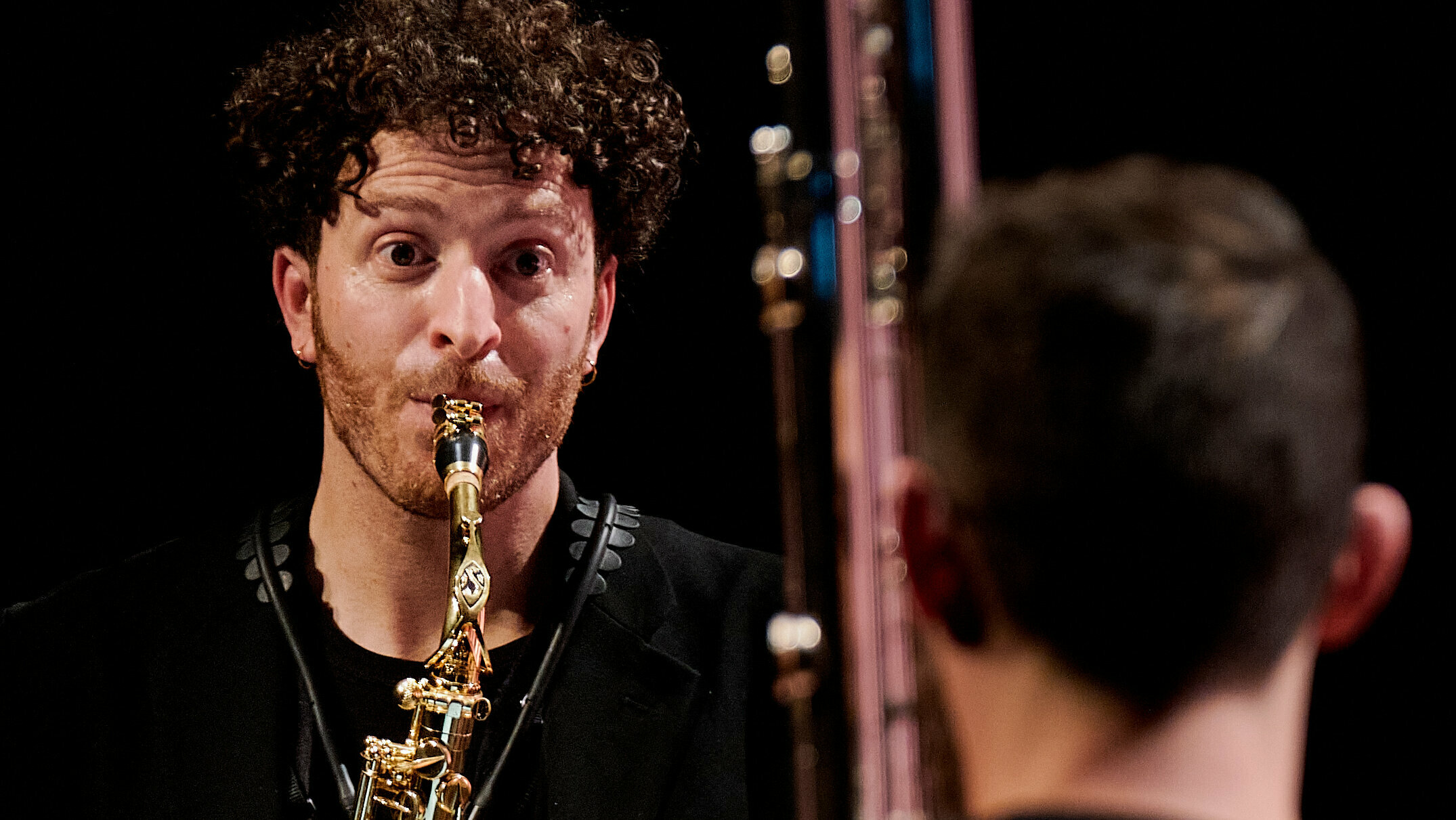 Ein Musiker spielt Saxophon mit Blick auf einen weiteren Musiker