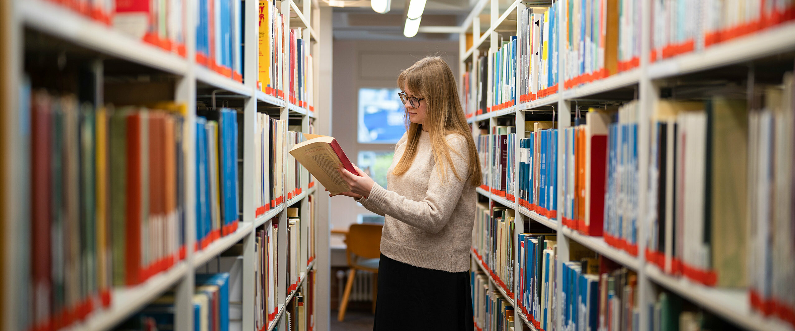 Eine Studentin schaut in der Bibliothek in ein Buch