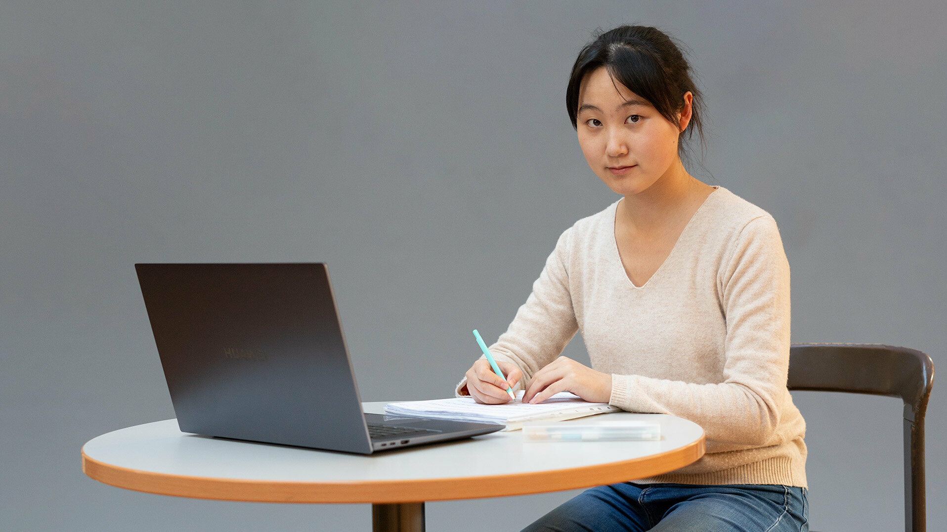 Eine junge Frau sitzt schreibend an einem Tisch mit Laptop